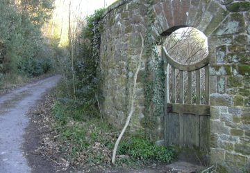 Closed wooden gate in a stone wall by a road.