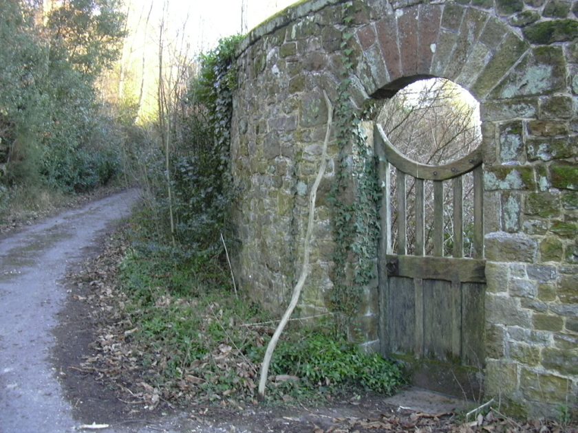 Closed wooden gate in a stone wall by a road.